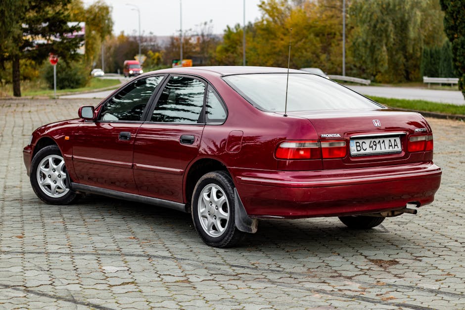 Red Honda Accord parked outdoors on cobblestone street in autumn.