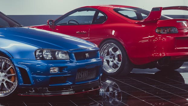 Blue Nissan Skyline GT-R and red Toyota Supra parked in a showroom.