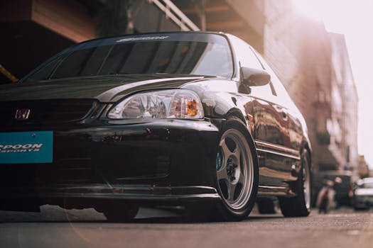 Low angle view of a modified black Honda Civic parked on a city street with sunlight flare.