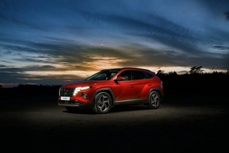 Red Hyundai Tucson SUV parked at sunset on an open road.