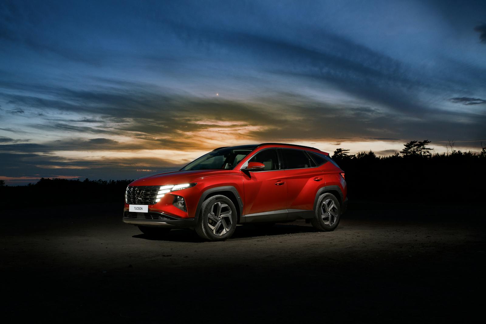 Red Hyundai Tucson SUV parked at sunset on an open road.