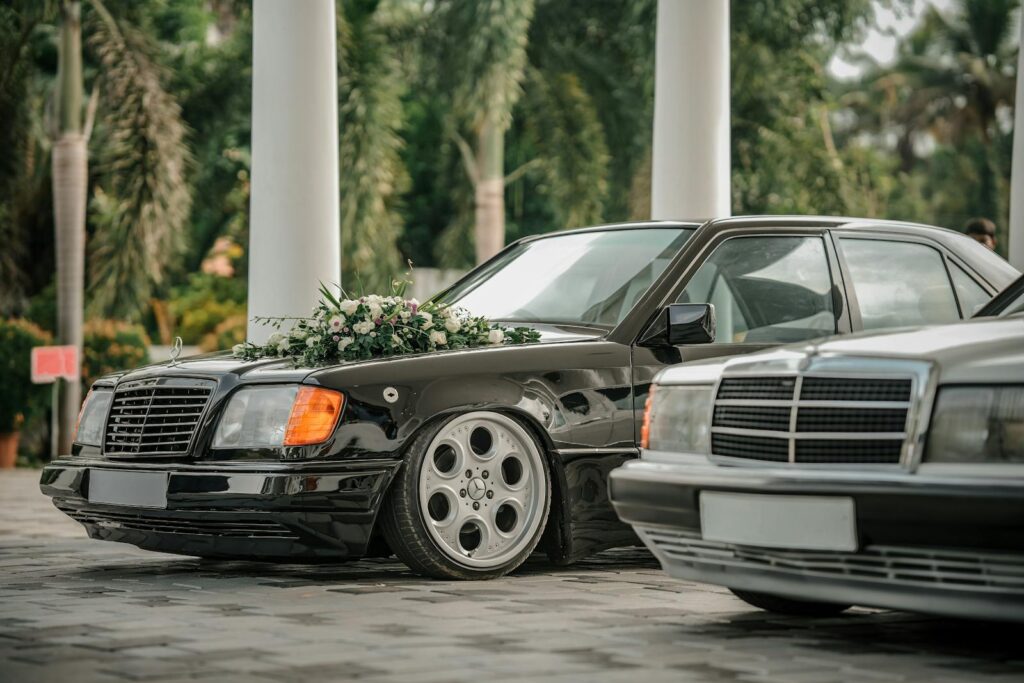 Close-up of a vintage black car adorned with floral decorations, set outdoors for a wedding ceremony.