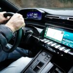 A detailed view of a car's interior with hands on the steering wheel, showcasing modern technology.