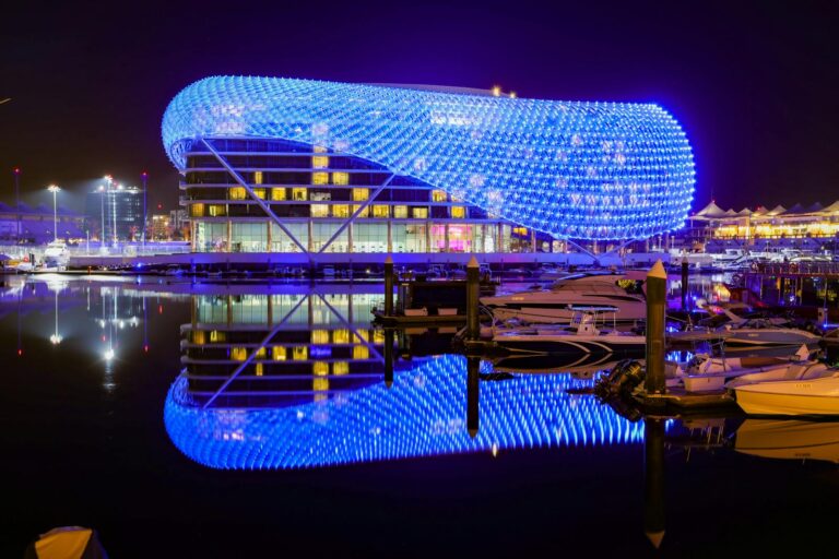 Modern hotel with vibrant blue lights reflecting in calm waters at night.