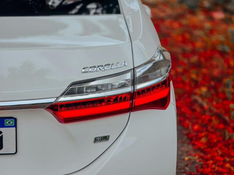 Close-up of a white car's back with bright red taillight surrounded by autumn leaves.