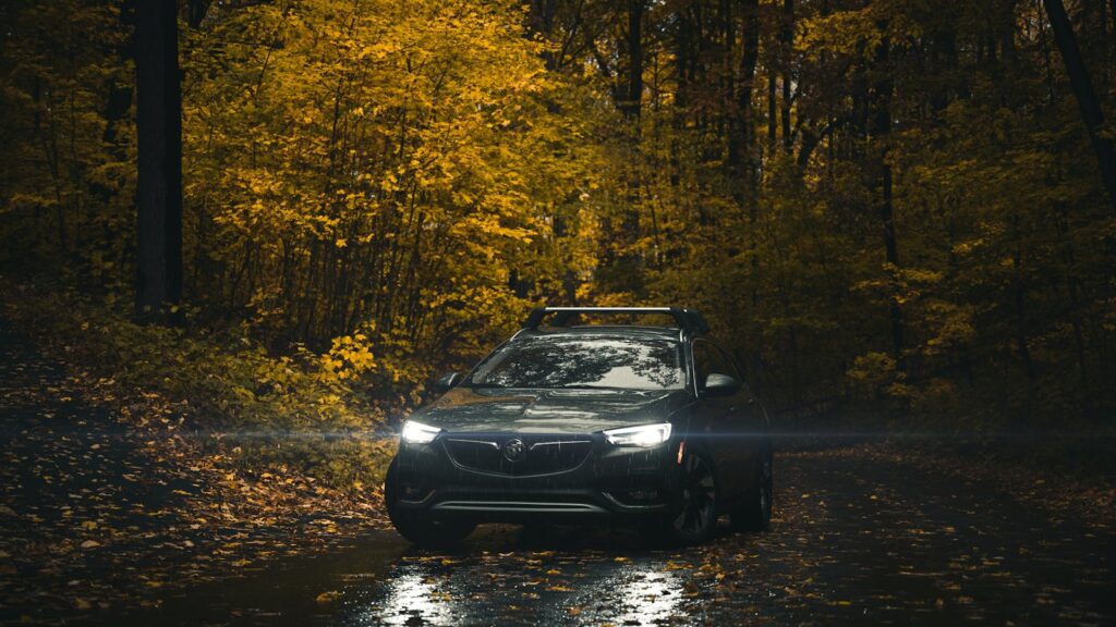 A Buick car with headlights on, driving through a scenic autumn forest road.