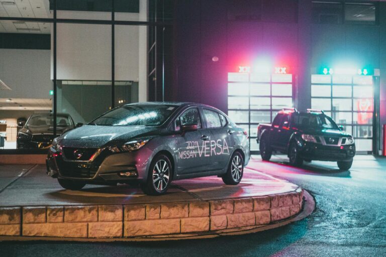 Urban showroom with luxury cars, illuminated by neon lights, showcasing modern vehicles at night.