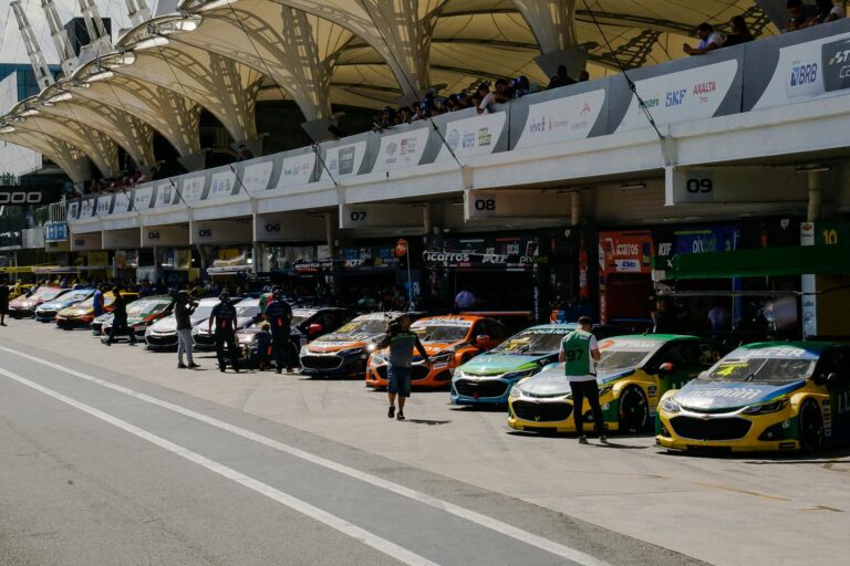 Stock cars lined up at the circuit garage during a sunny racing event.